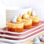 Mini Easter cheesecakes with a bird's nest of shredded coconut with candy eggs on a pink platter.