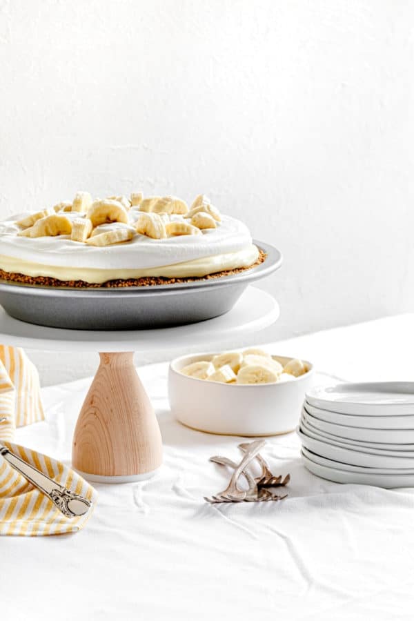 Banana pudding pie (AKA: Banana cream pie) on a dessert stand with plates and forks.