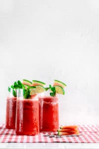 3 tall glasses of watermelon slushie with glass straws. Drinks are garnished with watermelon slices, mint and limes.