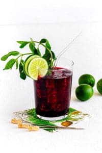 Ice cold glass of hibiscus tea (AKA Agua de Jamaica) garnished with mint, lime and straw.