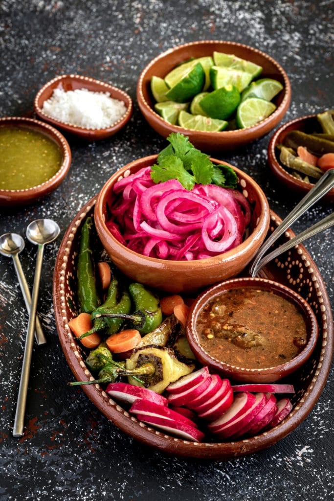 Mexican clay condiment tray with pickled red onions, salsa verde, salsa roja, and grilled chiles.