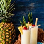 Two homemade pina colada. Glasses are garnished with pineapple, cherries and a bamboo straw.