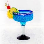 Blue Margarita in a Mexican bar glass garnished with orange slice, lime slice, and Maraschino cherry.
