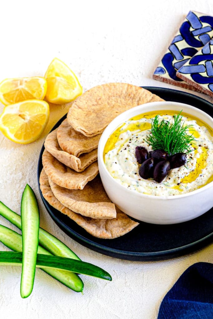 Greek gyro sauce in a white bowl alongside fresh pieces of pita bread.