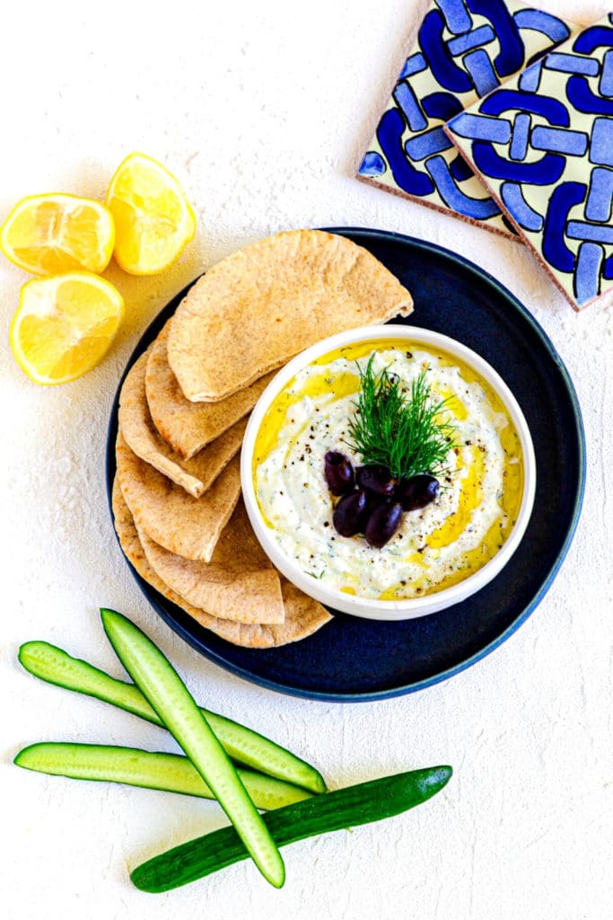 Tzitziki Sauce garnished with dill and Kalamata olives, served with pita bread on a blue platter.\