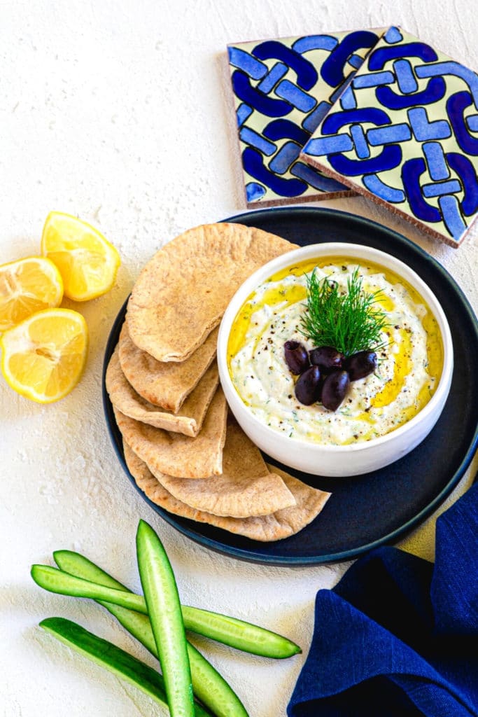 Tzatziki sauce in a white bowl served with flatbread and Greek olives.