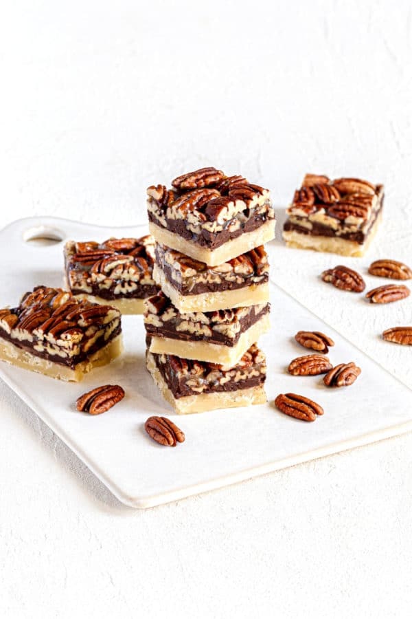 Stack of chocolate Pecan Pie Bars on a white ceramic serving board.