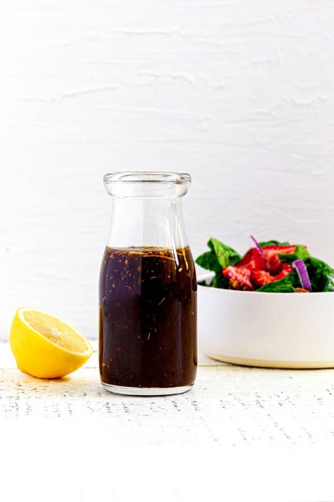 Creamy balsamic dressing in a glass jar next to a strawberry salad.