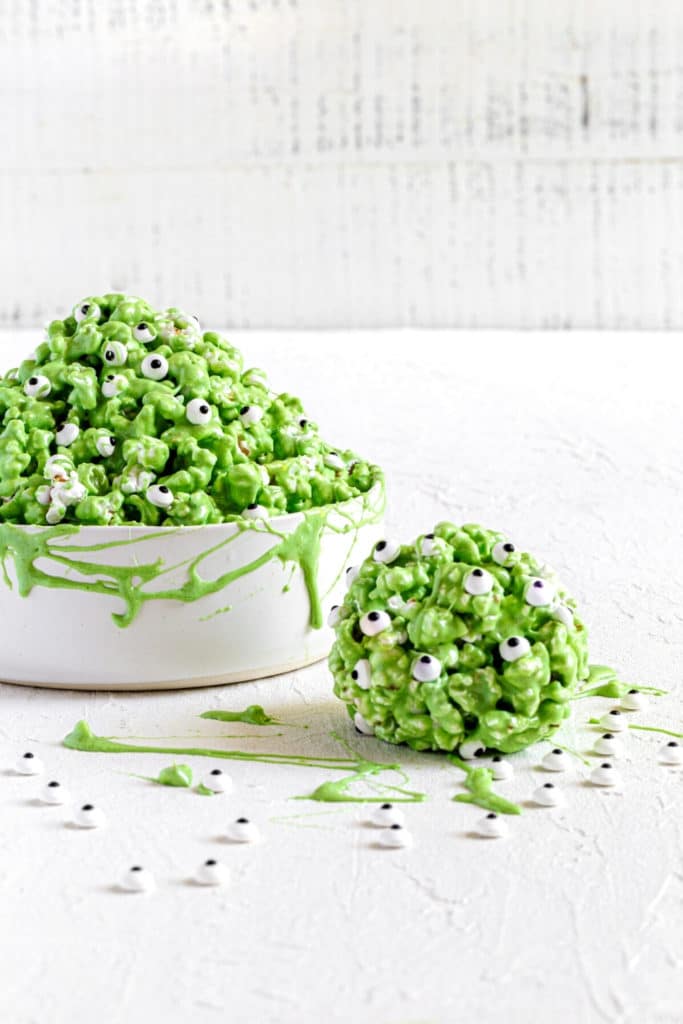 Green popcorn slime in white bowl with stretches of marshmallow slime and spooky candy eyes.