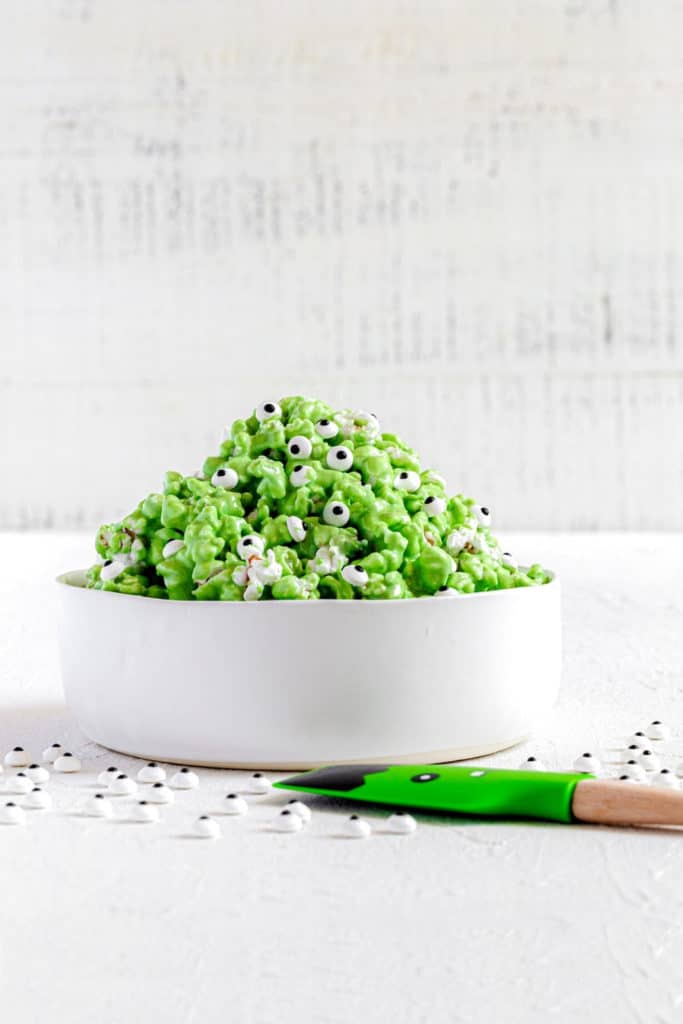 Monster popcorn with green marshmallow slime and googly eyes in a white serving bowl.