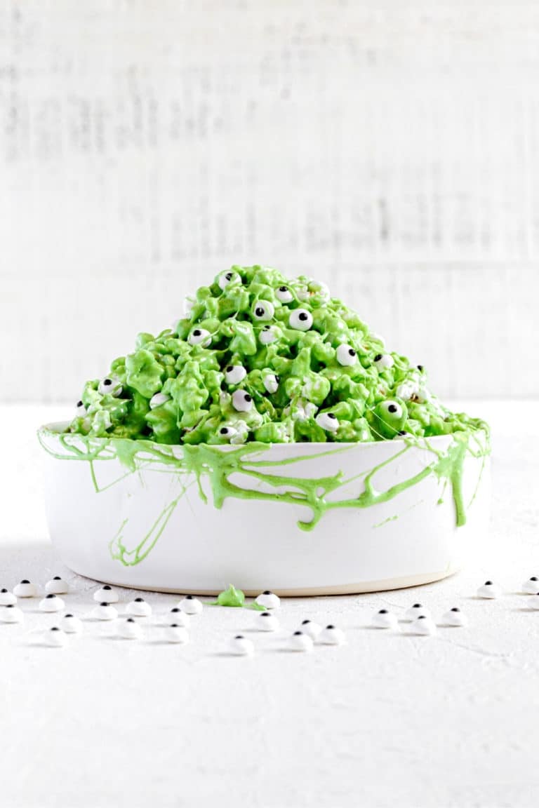 Green popcorn slime garnished with spooky candy eyes served in a white bowl.