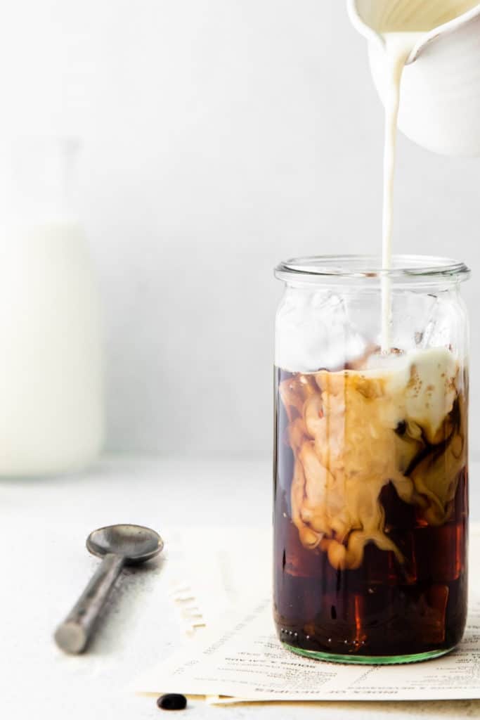 Iced Vanilla Latte in a Weck jar drinking glass with milk being poured in over ice.