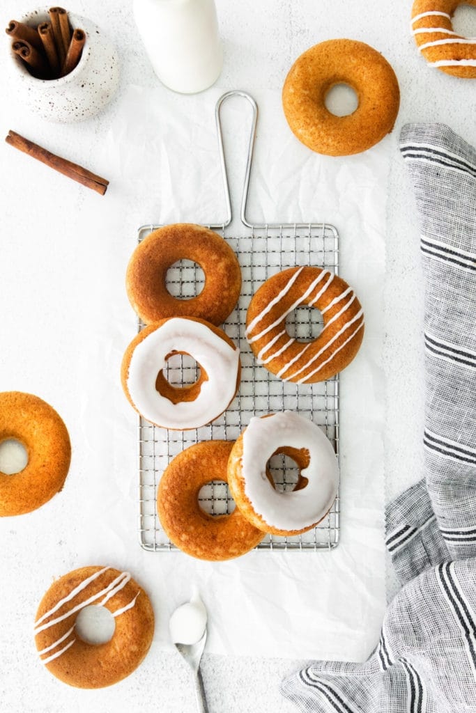 Freshly baked cinnamon donuts with vanilla glaze cooling on a wire rack.