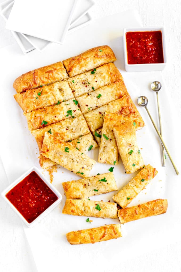 Cheesy Breadsticks with garlic butter served next to appetizer plates and bowls of marinara dipping sauce.