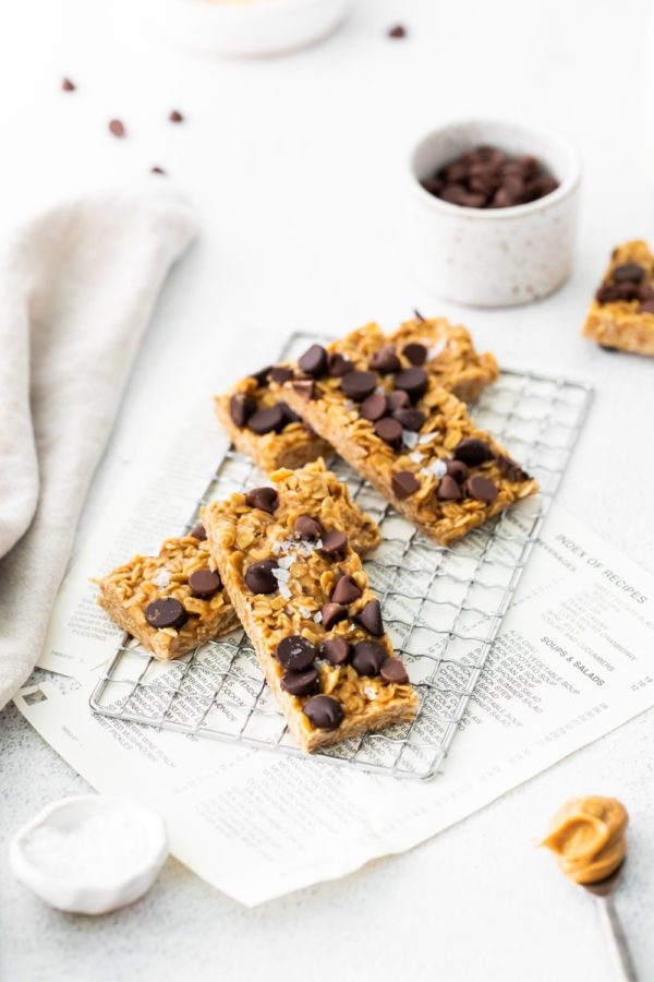 Four chewy granola bars topped with chocolate chips and flaky sea salt on a wire rack.