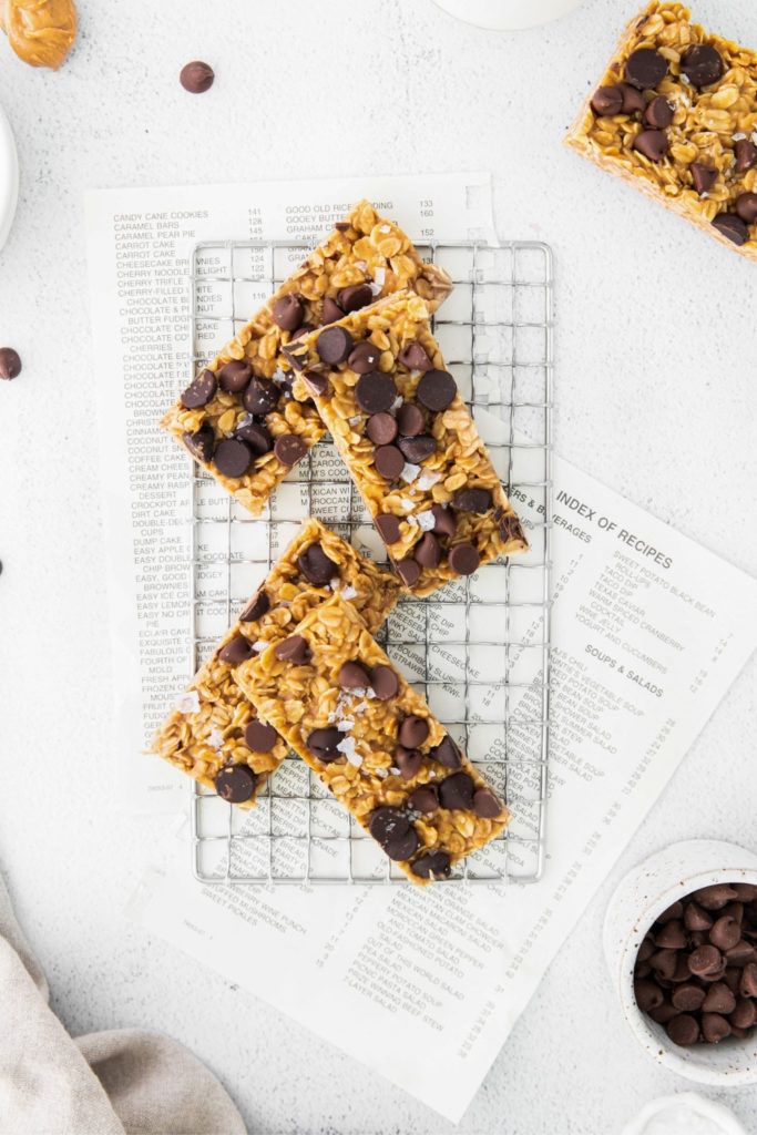 Chewy chocolate chip granola bars on metal rack over torn pages of a recipe book.
