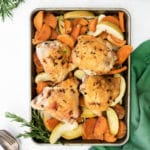 Chicken sweet potato bake sheet pan dinner with apples and rosemary on a tabletop with plates.