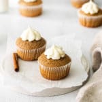 Cinnamon cupcakes with cream cheese frosting on a light-grey surface.