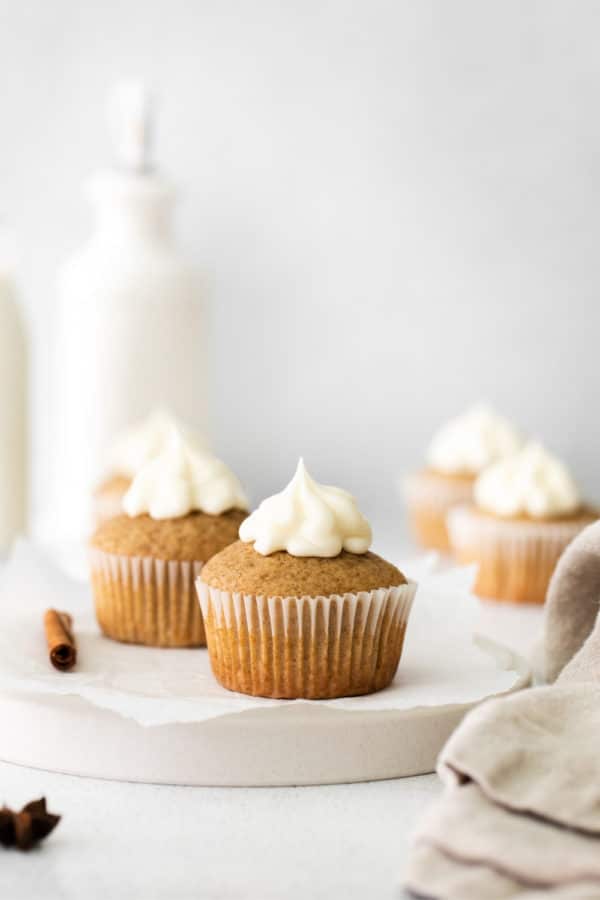 Cinnamon cupcakes with cream cheese frosting on top of a ceramic serving board with linen napkin.