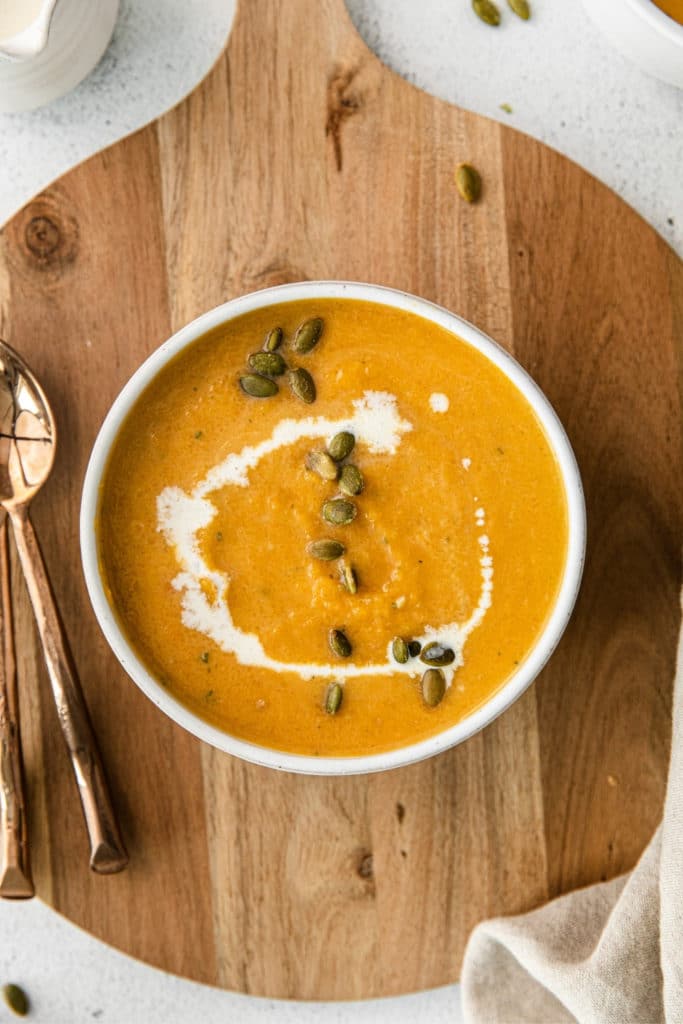 Healthy butternut squash soup drizzled with cream sprinkled with roasted pepitas, and served with a spoon.