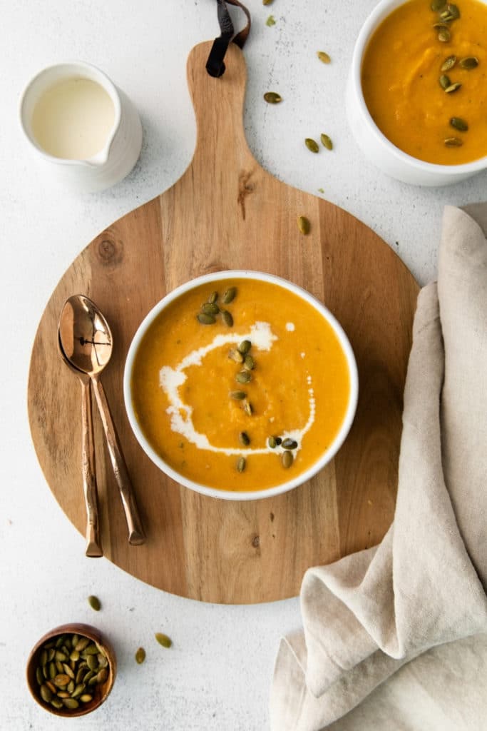 Bowl of creamy butternut squash soup drizzled with heavy cream and sprinkled with pumpkin seeds.