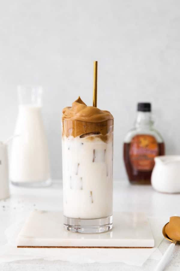 Tall glass of maple whipped coffee iced latte with gold straw on white marble coaster.
