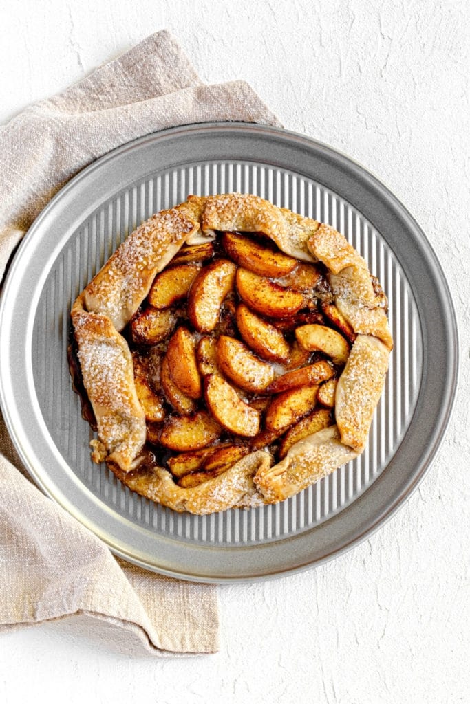 Homemade peach galette on round metal tray.