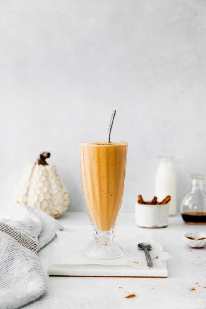 Pumpkin spice smoothie with frozen bananas served in a restaurant-style milkshake glass with metal straw.