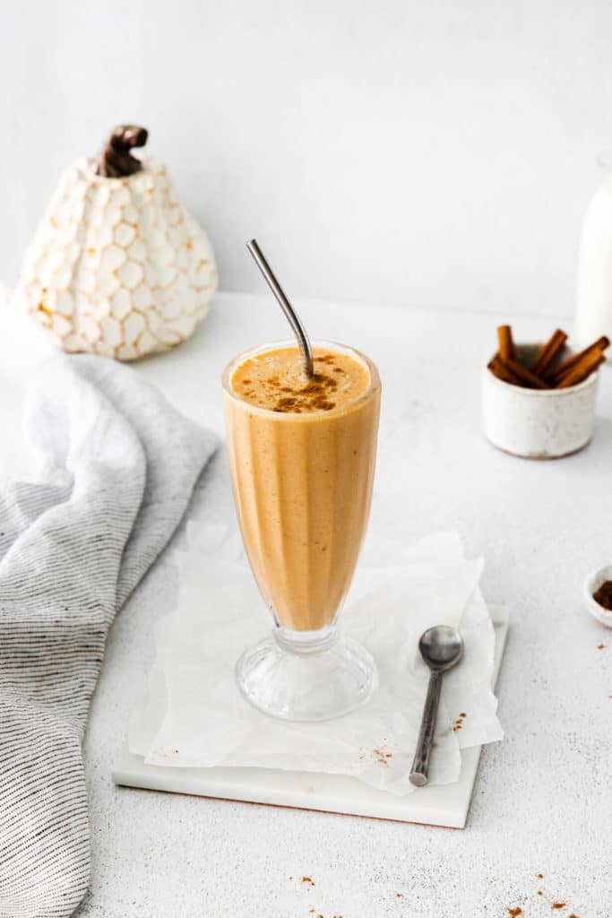 Pumpkin smoothie with frozen bananas served in a tall glass and garnished with pumpkin pie spice.