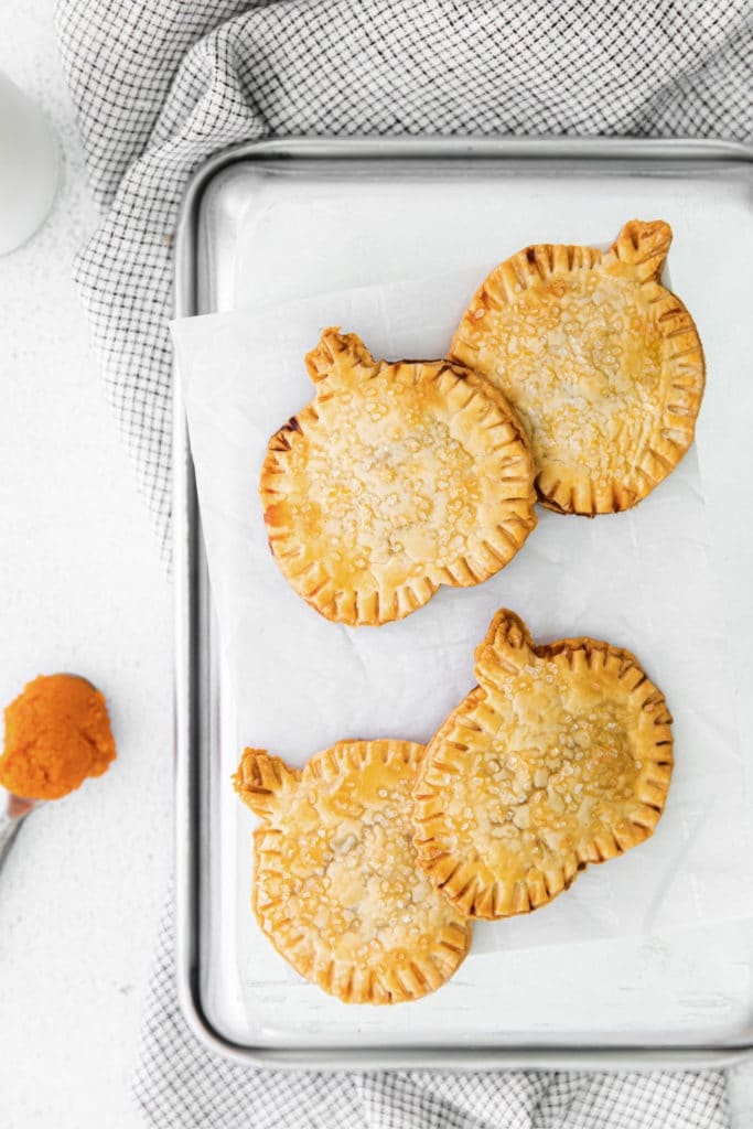 Pumpkin pie pop tarts in the shape of mini pumpkins sprinkled with sparkling sugar on a baking tray.
