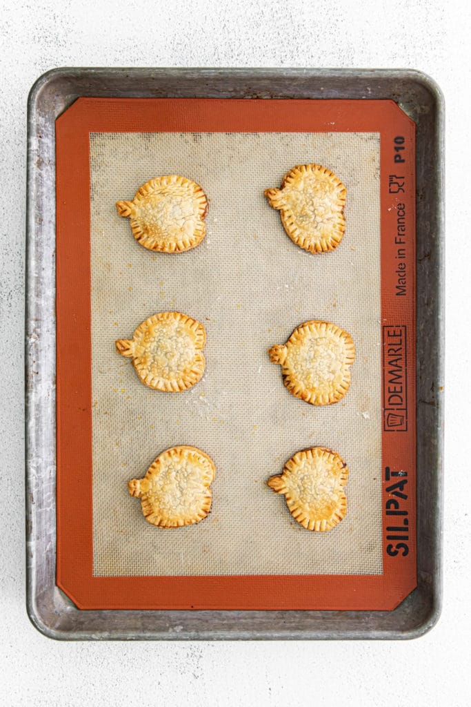 Six pumpkin pie pop tarts fresh out of the oven on a baking tray.