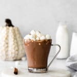 A warm cozy mug of pumpkin spice hot chocolate with mini marshmallows on top.