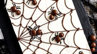 Slab of spiderweb chocolate bark on black stone serving tray surrounded by cloth cobwebs and spider.