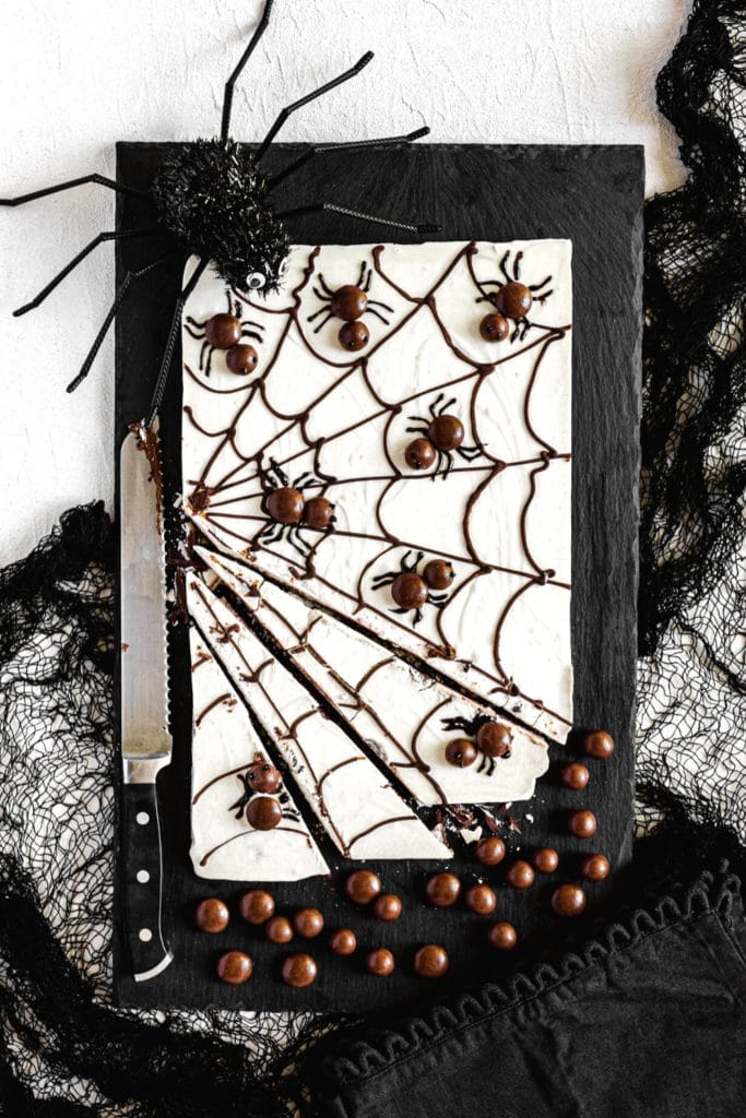 Slab of Halloween chocolate bark sliced into pieces with a serrated knife on a black board.