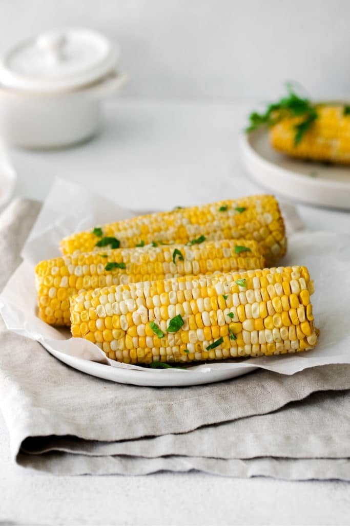 A white platter with 3 corn on the cob garnished with fresh parsley.