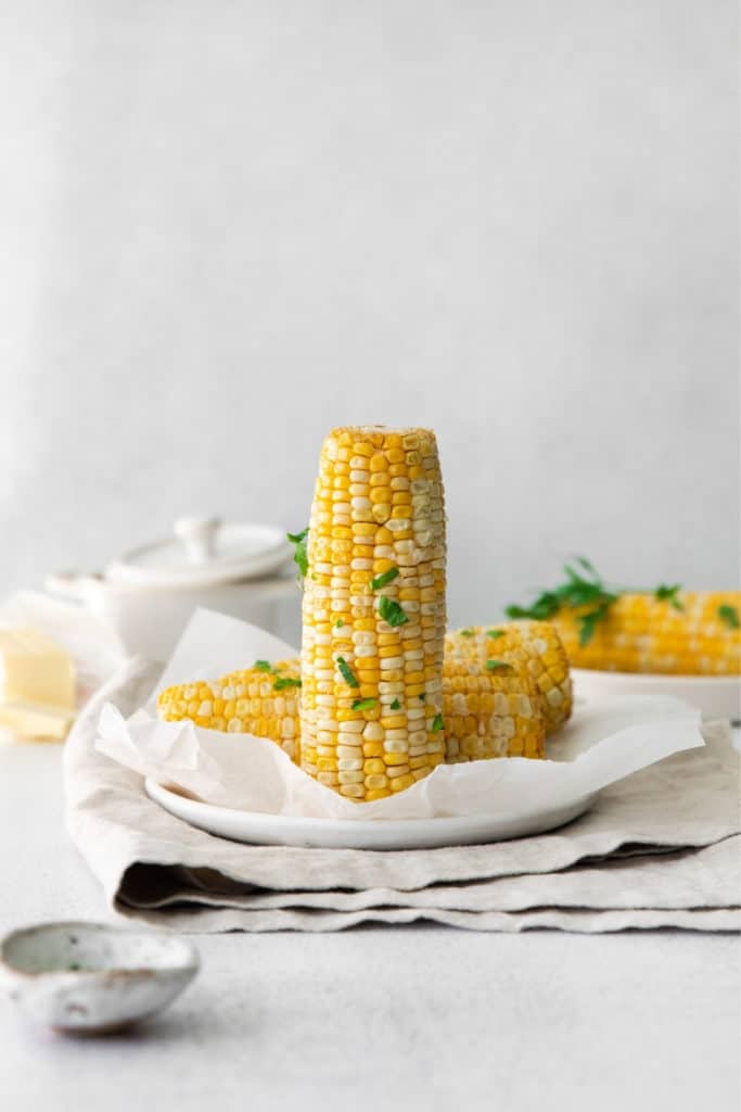 Air fryer corn on the cob garnished with butter, salt and fresh parsley.