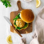 Overhead view of air fryer crab cake sandwich on a bun with produce, spread and lemon.
