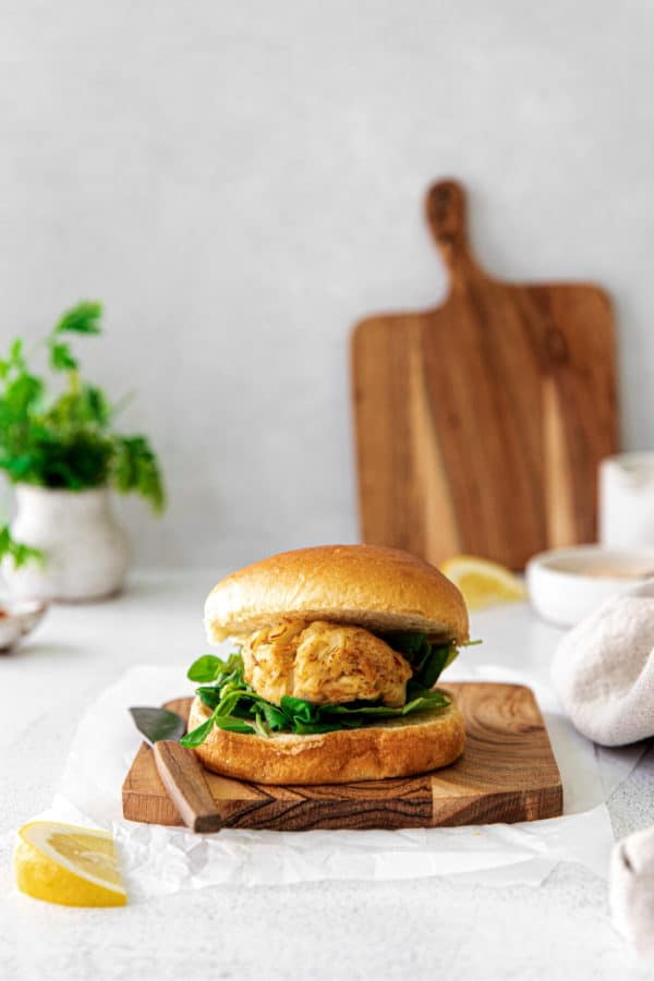 Air fryer crab cake sandwich on a wooden board with knife and wedge of juicy lemon.