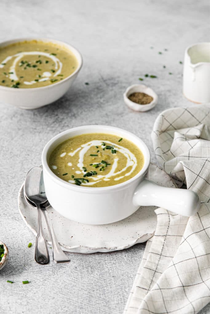 A serving of Cream of Asparagus Soup garnished with a swirl of heavy cream and sprinkling of chives.