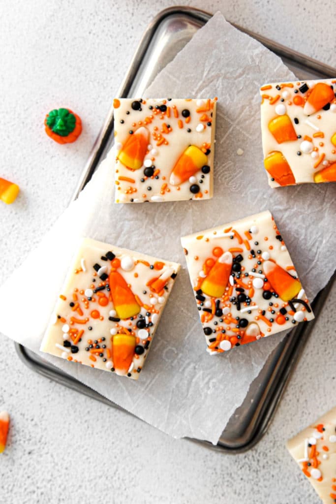 Four squares of white Halloween fudge with candy corn and Halloween sprinkles on a metal tray.