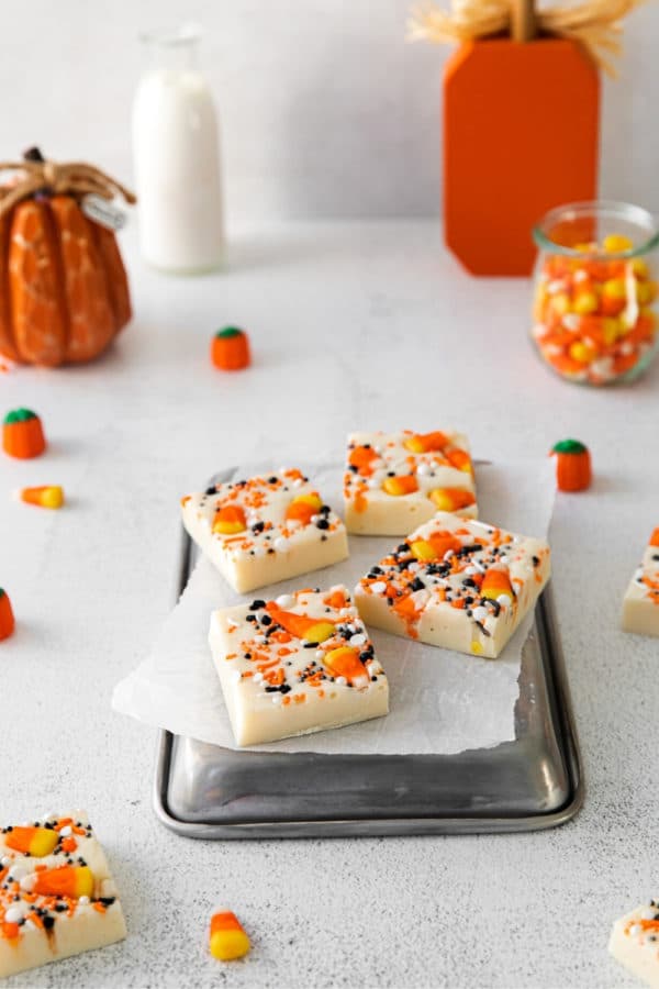 Four squares of Halloween candy corn fudge sitting on a small metal tray on a decorated dessert table.
