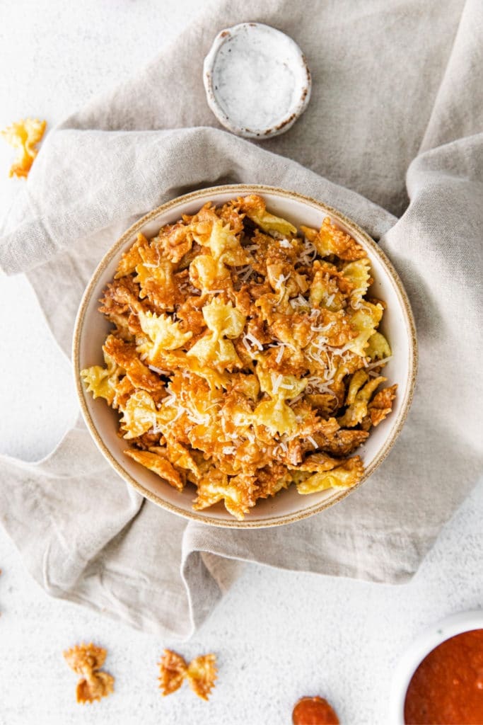 Garlic-parmesan pasta chips in a bowl alongside marinara dipping sauce.