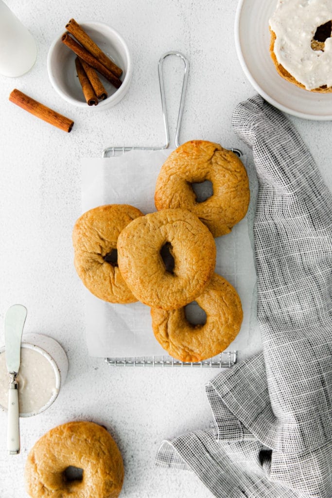 A half dozen pumpkin bagels on a serving table with maple cream cheese spread.