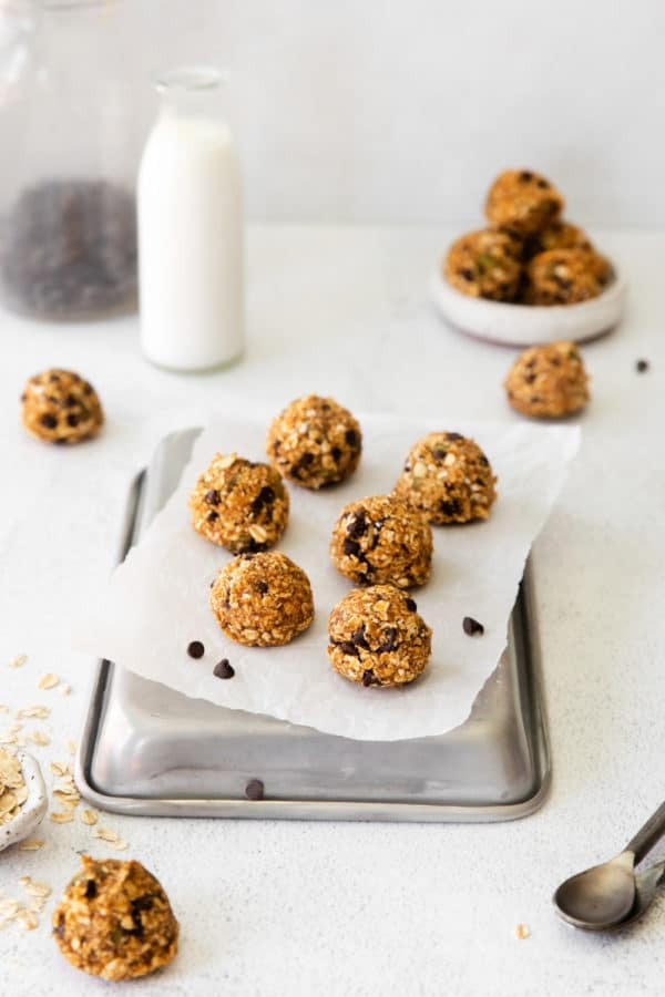 One dozen pumpkin energy balls with oats and chocolate chips on a snack table with milk.