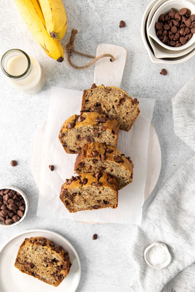 Five slices of banana bread with chocolate chips on a serving board with milk.