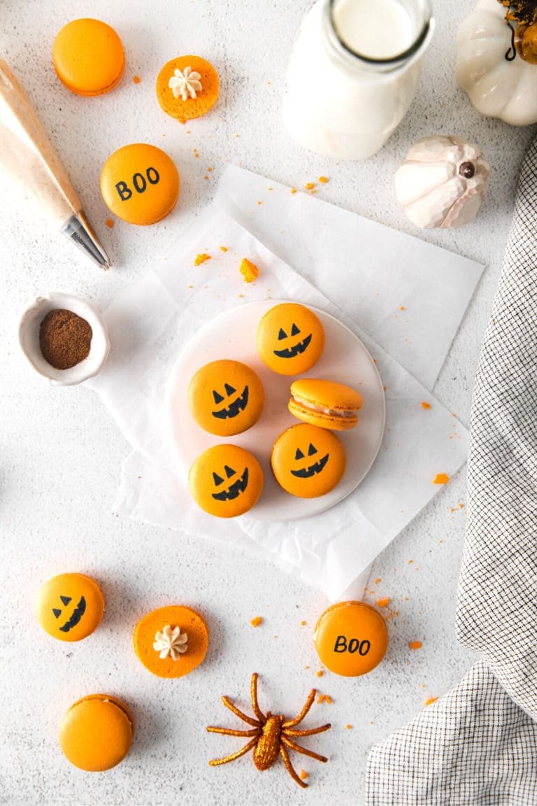 Orange Halloween pumpkin macarons with Jack-o'-lantern faces drawn in edible black ink.