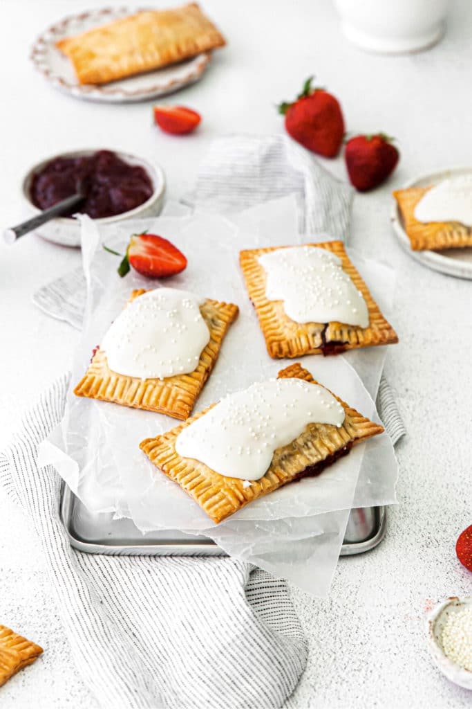 Three homemade strawberry pop tarts cooling on the back of a parchment paper-lined metal tray.