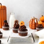 Chocolate pumpkin Thanksgiving cupcakes with chocolate buttercream frosting on a decorated Friendsgiving dessert table with milk.