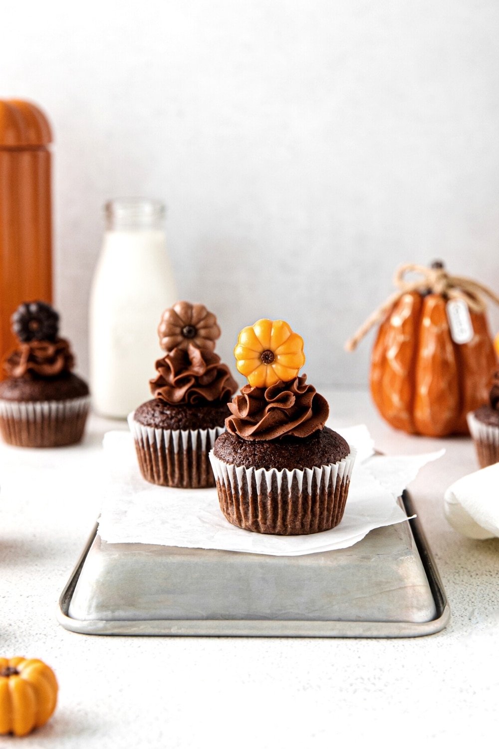 Three chocolate-pumpkin Thanksgiving cupcakes with chocolate buttercream frosting and decorative pumpkin cupcake toppers.