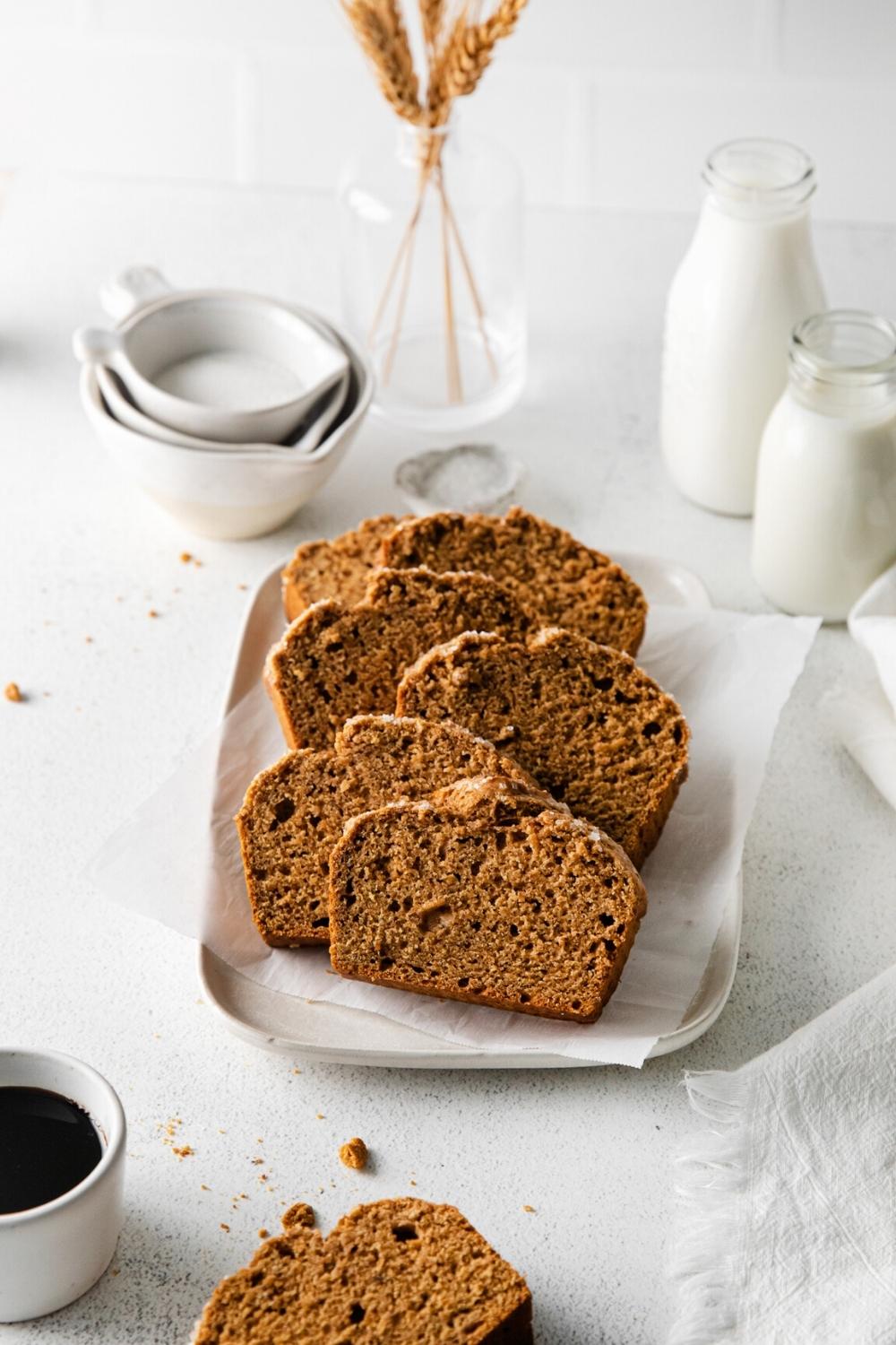 Sliced gingerbread loaf on a white platter next to glass bottles of milk and coffee.
